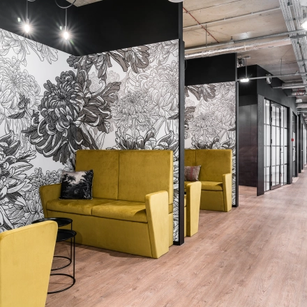 Modern office space in Warsaw's Śródmieście featuring stylish yellow seating, floral wall art, and a sleek hallway enhancing the office space rental experience.