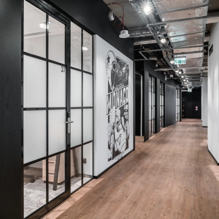 A modern office hallway with wooden flooring and glass-partitioned rooms at Plac Trzech Krzyży in Warsaw Śródmieście, perfect for office space rental.