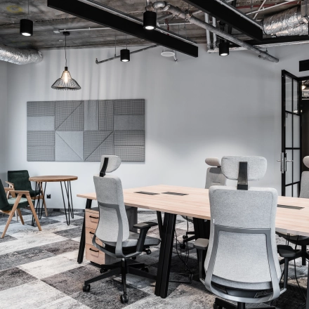 A modern furnished office space in Warsaw's Śródmieście at Plac Trzech Krzyży 10/14, featuring stylish workstations under exposed ceilings, ideal for office space rental.