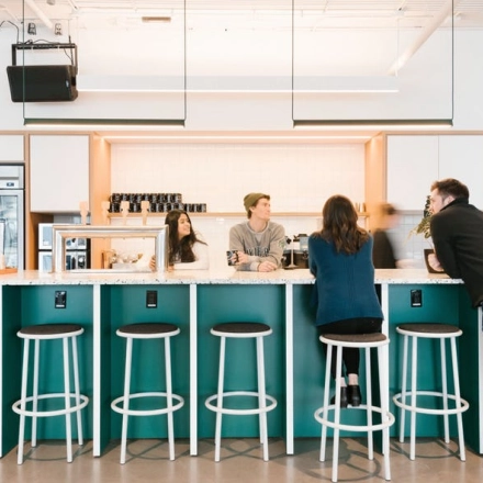 Modern office space with a group of people engaged in a casual meeting around a bar-style counter, perfect for office space rental in Warsaw Wola.