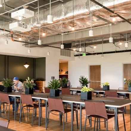 Modern office space rental in Warsaw Wola at Grzybowska 60 featuring open workspaces with stylish lighting and plants, two individuals working at separate tables.