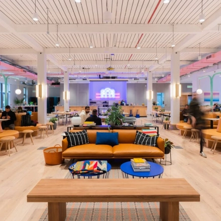 Spacious and modern office space with a vibrant atmosphere at Rondo Daszyńskiego 2, Warsaw Wola. People are working collaboratively on laptops around stylish tables, ideal for office space rental.