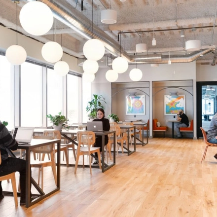 Spacious and modern office space rental at Rondo Daszyńskiego 2, Warsaw Wola, features people working on laptops at stylish wooden tables.