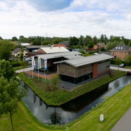 Aerial view of a modern office building for rent surrounded by greenery and a canal at M.A. Reinaldaweg 2d, Woerden. The architecture features sleek lines and a practical design, ideal for professional use.