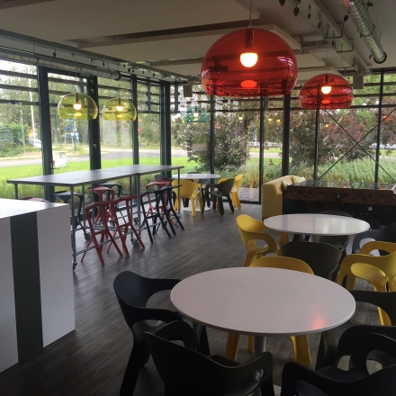 A modern, furnished office space with colorful seating and large windows in Woerden, ideal for rent office space seekers. The room is bright and versatile, featuring communal tables and comfortable chairs.