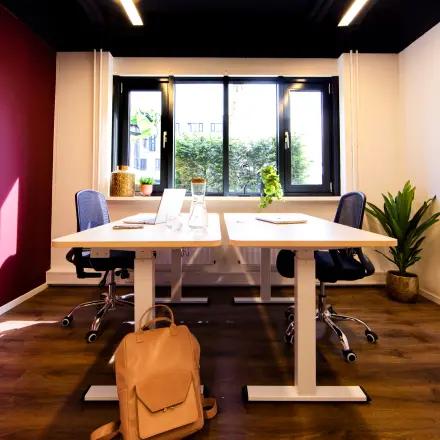 Well-lit office space at Pelmolenlaan 16, Woerden, featuring two desks with chairs, ideal for rental. The room has vibrant decor and large windows offering natural light.