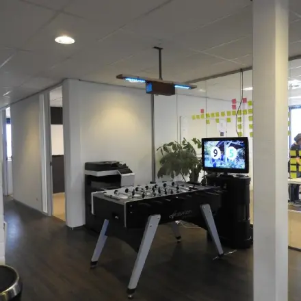 Office with a foosball table, TV displaying a sports score, and office equipment at Pompmolenlaan 9, Woerden, available for rent.