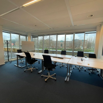Spacious office to rent at Baron de Coubertinlaan 35, Zoetermeer, featuring a large table with chairs, ready for meetings. Ideal for office space rental with expansive windows letting in natural light.