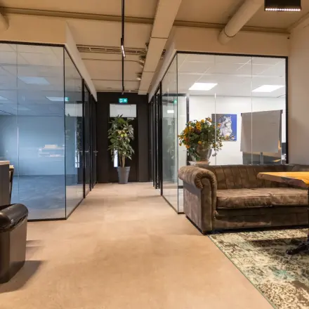 Office to rent at Boerhaavelaan 40 in Zoetermeer featuring a cozy furnished interior with a sofa and a wooden table, surrounded by glass-walled rooms and decorative plants.