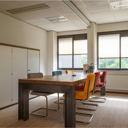 Bright, furnished office space available for rent at Bredewater 26, Zoetermeer, featuring a wooden table, diverse chairs, and large windows for natural light.