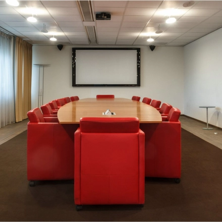 Spacious conference room with a large oval table surrounded by vibrant red chairs, ideal for productive meetings. Located in the office space rental at Bredewater 26, Zoetermeer.