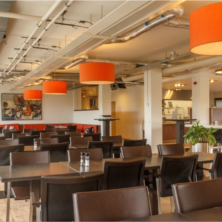 Spacious, furnished office space rental featuring a bright, open floor plan with modern tables and chairs, accent lighting, and art decor at Bredewater 26, Zoetermeer.