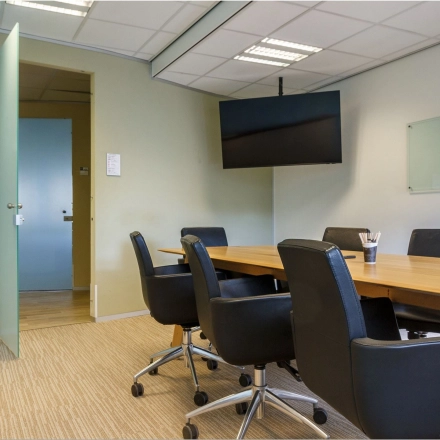 Conference room with a large wooden table, black chairs, and a wall-mounted TV, suitable for office space rental at Bredewater 26, Zoetermeer.