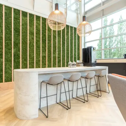 Modern office space available for rent in Zoetermeer, featuring a sleek lounge area with a marble counter, bar stools, and unique lighting fixtures.