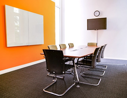 Modern conference room with an orange accent wall and a long table surrounded by chairs, located at Badenerstrasse 47 in Zürich Center. Ideal for office space rental.
