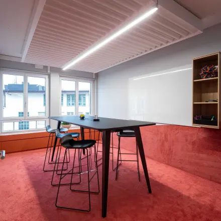 Stylish office space with a red carpet, high table, and modern stools, located at Talacker 41 in Zürich Center. Ideal for office to rent needs.