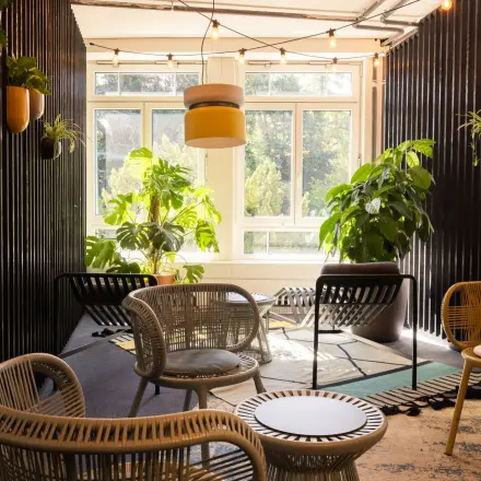 Bright lounge area at Talacker 41, Zürich Center, featuring rattan furniture and large windows with potted plants, ideal for a relaxed office space rental.