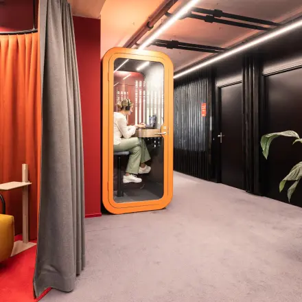 Colorful office hallway with a private phone booth, rent office space in Talacker 41, Zürich Center. Decor includes seating and large plant.