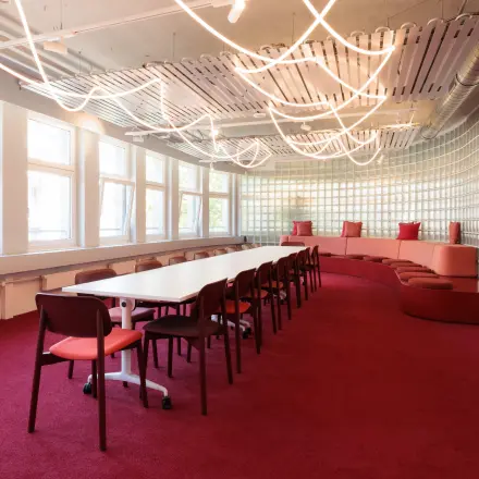 Bright office at Uraniastrasse 31 in Zürich Center features a long table and chairs, ideal for office space rental. Unique lighting and a cushioned seating area enhance the workspace environment.