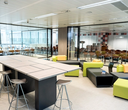 Moderna oficina en Carrer de Llull 321, Barcelona, con mobiliario colorido y espacios abiertos ideales para alquilar una oficina. El ambiente es luminoso y está preparado para reuniones y trabajo colaborativo.