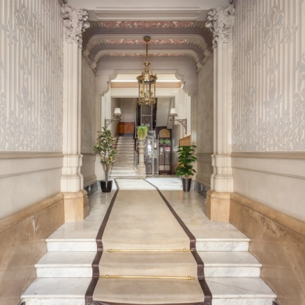 Entrada elegante y señorial para alquilar una oficina en Barcelona Eixample, Rambla de Catalunya 125, con suelo de mármol y detalles ornamentales en las paredes.