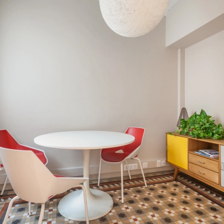 Espacio de trabajo iluminado y acogedor en alquiler de oficinas en Rambla de Catalunya, Barcelona Eixample, con mesa redonda, sillas rojas y suelo de mosaico.