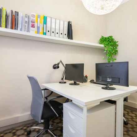 Espacio de trabajo luminoso ideal para alquilar una oficina en Rambla de Catalunya 125, Barcelona Eixample, con escritorio ordenado, silla ergonómica y estantería con documentos.