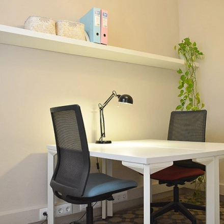 Oficina luminosa y equipada en alquiler de oficinas en Rambla de Catalunya 125, Eixample, Barcelona, con escritorio, sillas y estantería.