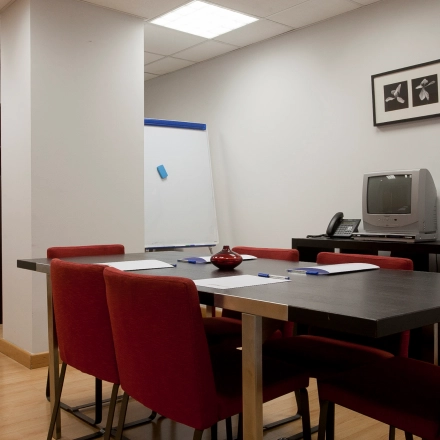 Oficina en alquiler ubicada en Calle Lagasca 95, Madrid Salamanca, equipada con mesa de reuniones, sillas rojas y un mueble con televisión.