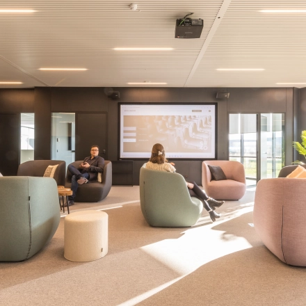 Moderne kantoorruimte op Korte Keppestraat 19 in Aalst met comfortabele zitmeubels en een groot presentatiescherm. Mensen zijn bezig met werkbesprekingen in deze lichte en uitnodigende omgeving.