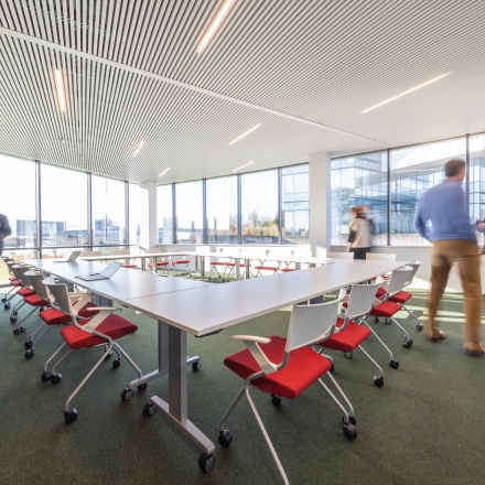 Zakelijke professionals voeren activiteiten uit in een lichte en moderne kantoorruimte met uitzicht op de stad in Aalst. De ruimte heeft stoelen en lange tafels, ideaal voor vergaderingen of teamwerk.