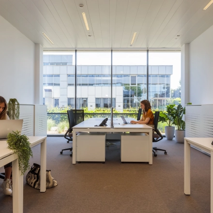 Kantoorruimte huren in Aalst met grote ramen en moderne inrichting, waar twee personen aan bureaus werken op laptops.