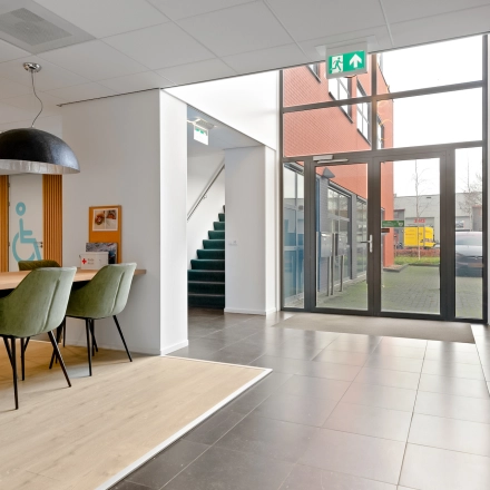 In de lichte entree van het kantoorpand aan de Jool Hulstraat 2-14 in Almere Stad staan groene stoelen bij een houten tafel. De kantoorruimte is geschikt om te huren.