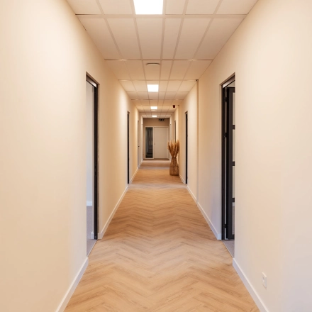 Heldere gang in het kantoorpand op Jool Hulstraat 2-14 in Almere Stad, met houten vloer en meerdere deuren naar kantoorruimtes.