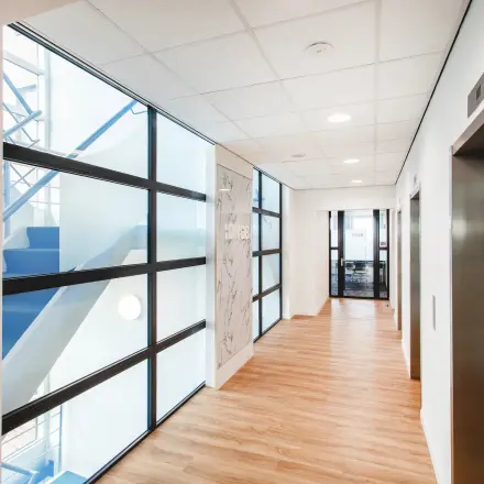 Lichte gang met houten vloer en glazen panelen in een kantoorpand aan de Landdrostdreef 124, ideaal voor kantoorruimte huren in Almere Stad.