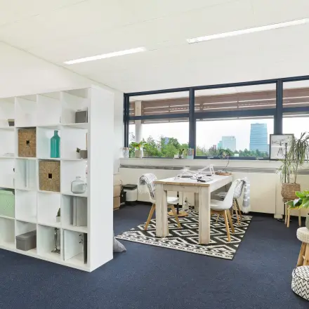 Lichte kantoorruimte met grote ramen en zicht op Almere Stad, voorzien van vergadertafel en decoratieve elementen. Geschikt voor werkruimte of vergaderruimte voor wie kantoorruimte wil huren.