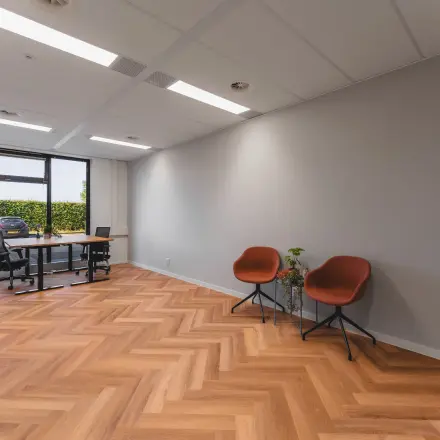 Moderne kantoorruimte te huur in Almere Stad met grote ramen, houten vloer en enkele meubels, ideaal voor zakelijke activiteiten.