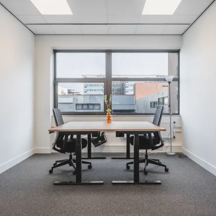 Kantoorruimte te huur in Almere Stad, Veluwezoom 15, met twee bureaus en stoelen onder een raam met uitzicht op naastgelegen kantoorpanden.