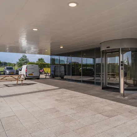 Entree van Veluwezoom 15 in Almere Stad met een draaideur en zitgelegenheid buiten. Ideaal voor bedrijven die op zoek zijn naar kantoorruimte om te huren.