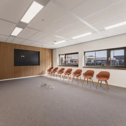 Moderne kantoorruimte op Veluwezoom 15 in Almere Stad met strakke lijnen, houten accenten en een rij stijlvolle stoelen langs de muur. Klaar voor vergaderingen of flexibele werkplekken.