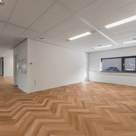 Ruime kantoorruimte met een houten visgraatvloer en veel natuurlijk licht dankzij een groot raam. Ideaal voor bedrijven die kantoorruimte willen huren aan de Veluwezoom 15 in Almere Stad.