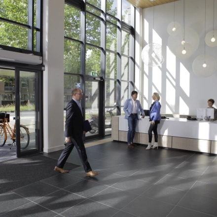 Moderne kantoorruimte op Europalaan 16 in Alphen aan den Rijn met een lichte ontvangsthal en glazen gevel. Mensen wisselen zakelijke ideeën uit bij de balie in een gemeubileerd kantoorpand.
