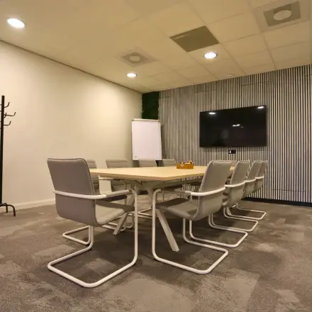 Moderne vergaderruimte in kantoorpand Leidse Schouw 2, Alphen aan den Rijn, met groot scherm, tafel en stoelen. Ideale plek om kantoorruimte te huren voor meetings. Groenaccenten en flip-over aanwezig.