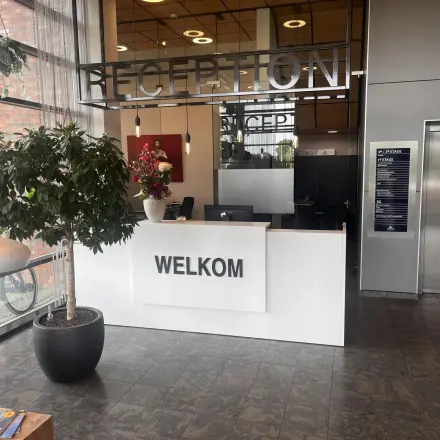 Moderne receptie in een kantoorpand op Leidse Schouw 2, Alphen aan den Rijn, met een balie, planten en kunst. Ideaal voor wie kantoorruimte wil huren.