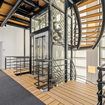 Moderne kantoorruimte met glazen lift, houten vloerdelen en stalen trap op Maanlander 43, Amersfoort Calveen, ideaal voor kantoorruimte huren.