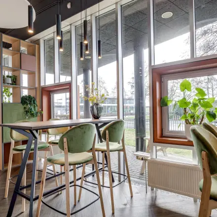 Moderne kantoorruimte huren in kantoorpand Maanlander 47, Amersfoort Calveen. Grote ramen laten veel licht binnen, met groen en hoge tafels in een uitnodigende omgeving.