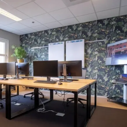 Gezellige kantoorruimte met moderne werkplekken, voorzien van beeldschermen en een inspirerende wand met plantenprint. Ideale locatie voor kantoorruimte huren in Amersfoort Centraal Station.