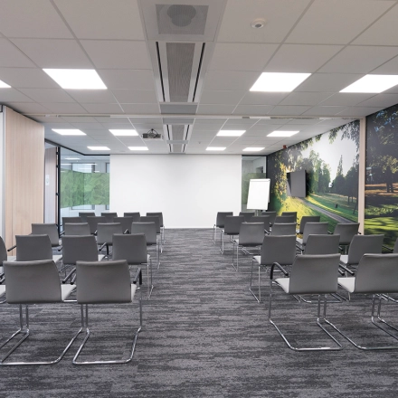 Moderne vergaderruimte met grijze stoelen en glazen wanden, geschikt voor kantoorruimte huren. Grote ramen laten veel licht binnen en er is een scherm voor presentaties.
