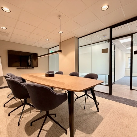 Moderne, goed verlichte vergaderruimte in een kantoorpand aan Professor E.M. Meijerslaan 1, Amstelveen, met comfortabele stoelen rondom een houten tafel en een presentatiescherm.