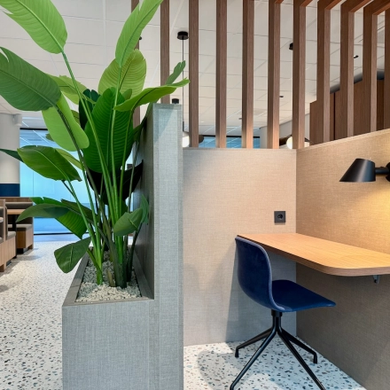 Moderne kantoorruimte met houten scheidingswanden, groene planten en een werkplek met een blauwe stoel. Ideaal om als kantoor te huren in Amstelveen, aan de Professor E.M. Meijerslaan 1.